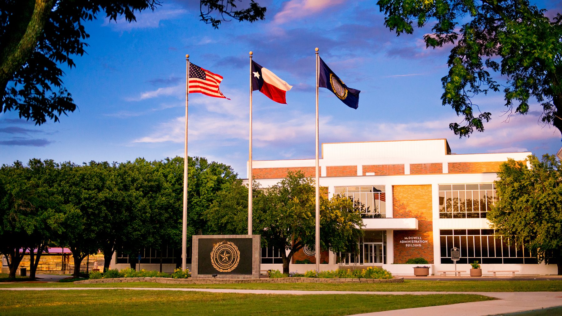 Three flag poles and the university symbol in front to the administration building on campus.