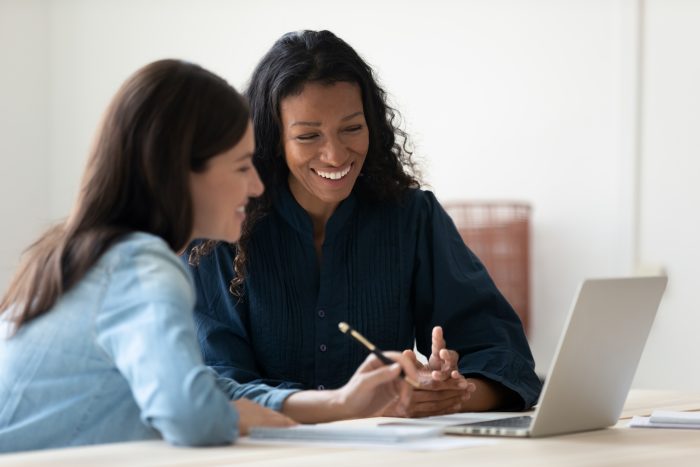 Close up happy young businesswoman using laptop with laughing female mentor