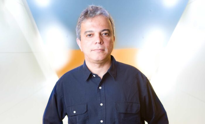 A man with gray hair wearing a navy-blue shirt poses confidently in a bright, softly lit space with gradient colors.