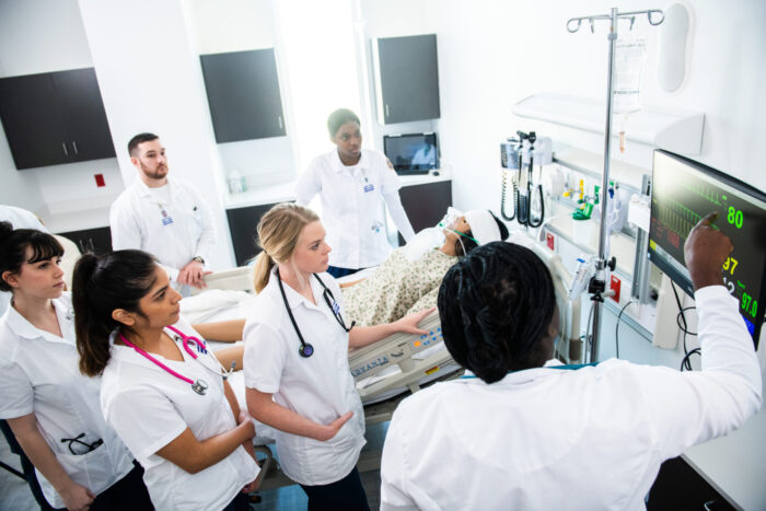 Future nurses studying patient life signs with teacher.