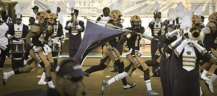a group of football player running to the field with a flag.