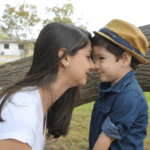 a female mother figure and a young boy touching noses and smiling at each other