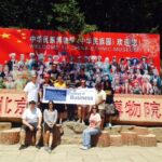 A group of students in front of an oriental red sign and with the university sign as well.