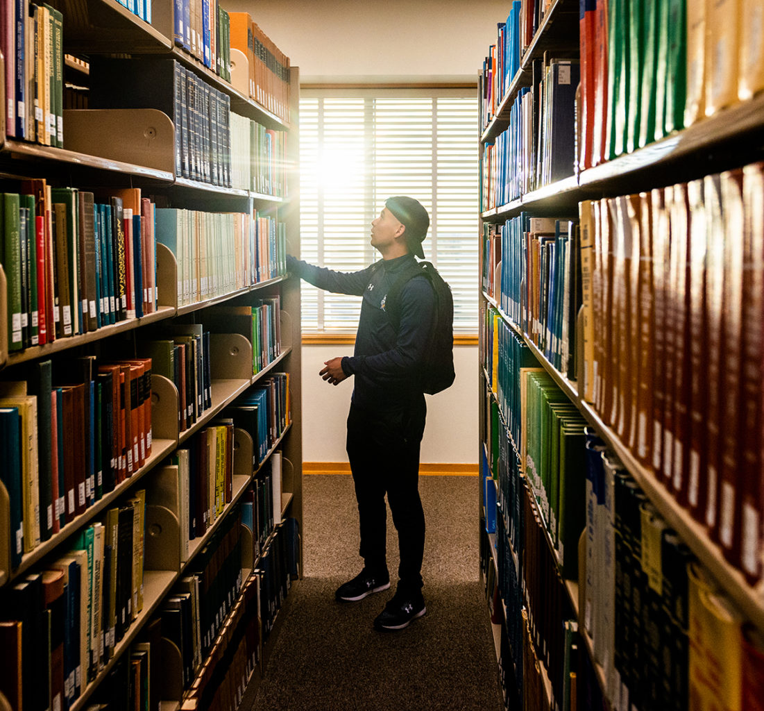 Male student looking for a book in the library.