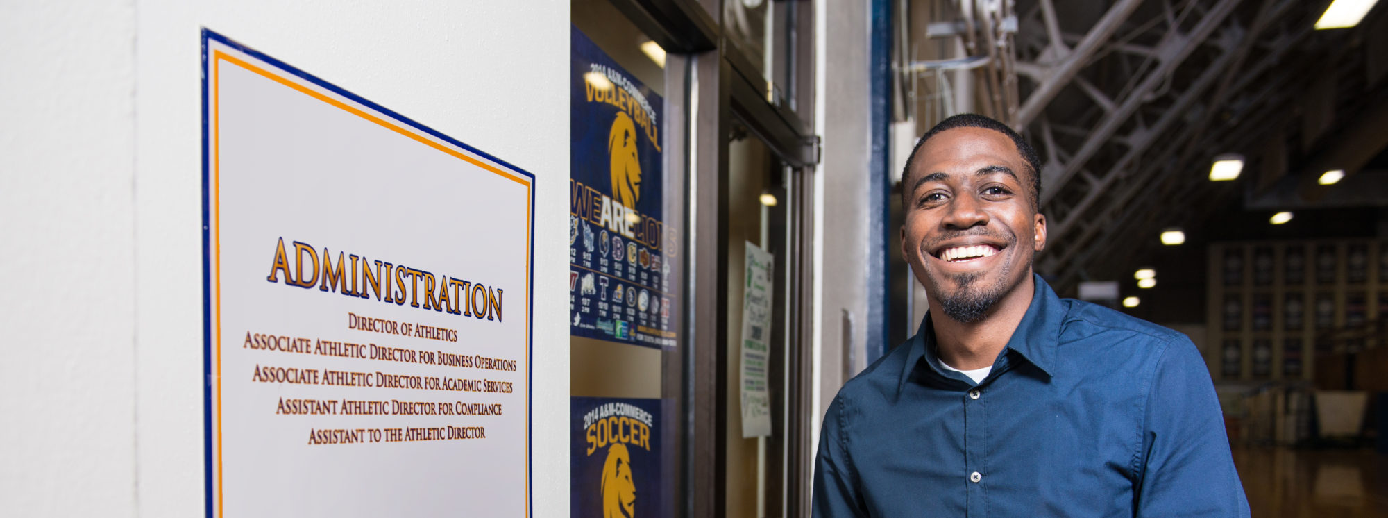 Athletic Administration Student smiling at the camera by the door of the ETAMU Athletics administration department.