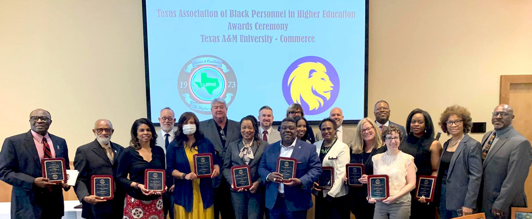 A group of people in formal attire pose for a photo, each holding a plaque.