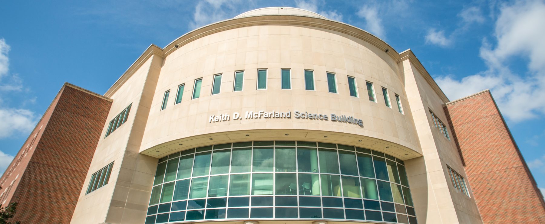 The image shows the Keith D. McFarland Science Building, featuring a modern facade with large glass windows and a rounded central structure.