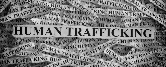 A collage of torn newspaper fragments displaying the text "HUMAN TRAFFICKING" repeatedly. The central, prominent piece highlights the term in bold, emphasizing the serious issue. The background pieces are slightly faded, drawing attention to the main focus.