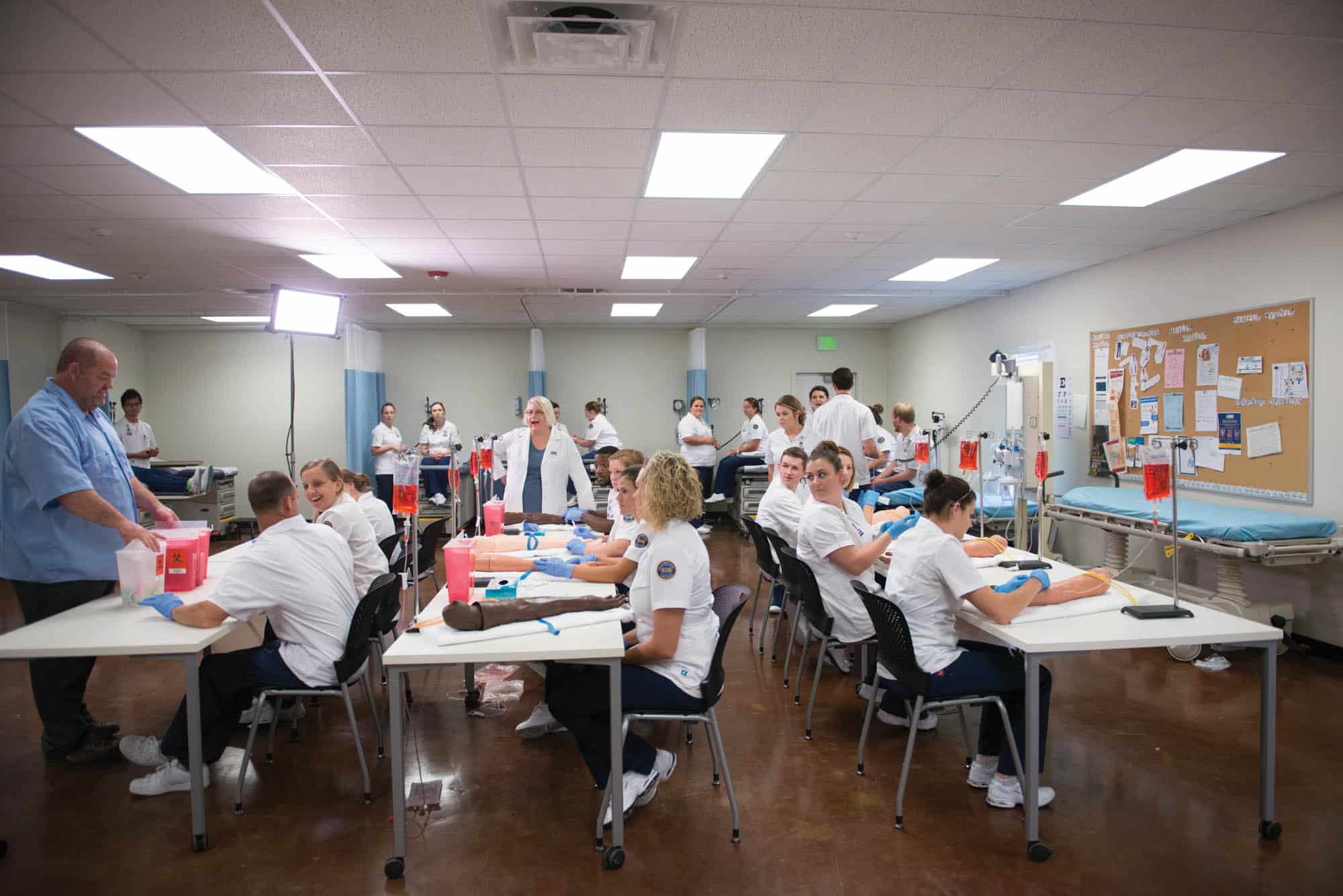 A group of nursing student in a classroom. It appears they are learning to draw out blood from an arm.