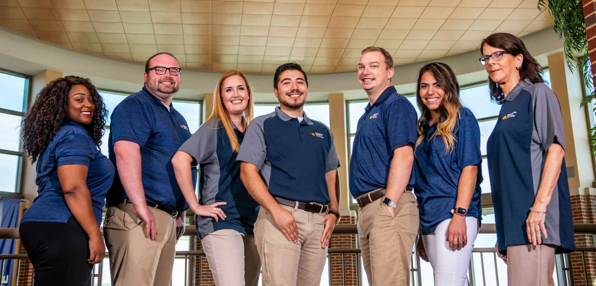 A group of 7 people standing in front of the camera man, smiling and posing.