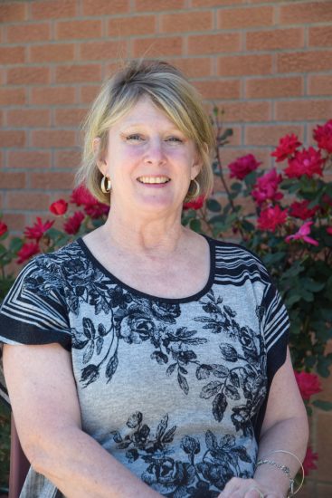 Connie Browning stands against a rose-vined exterior brick wall.