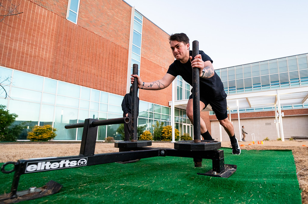 A man pushing strength training equipment outside.