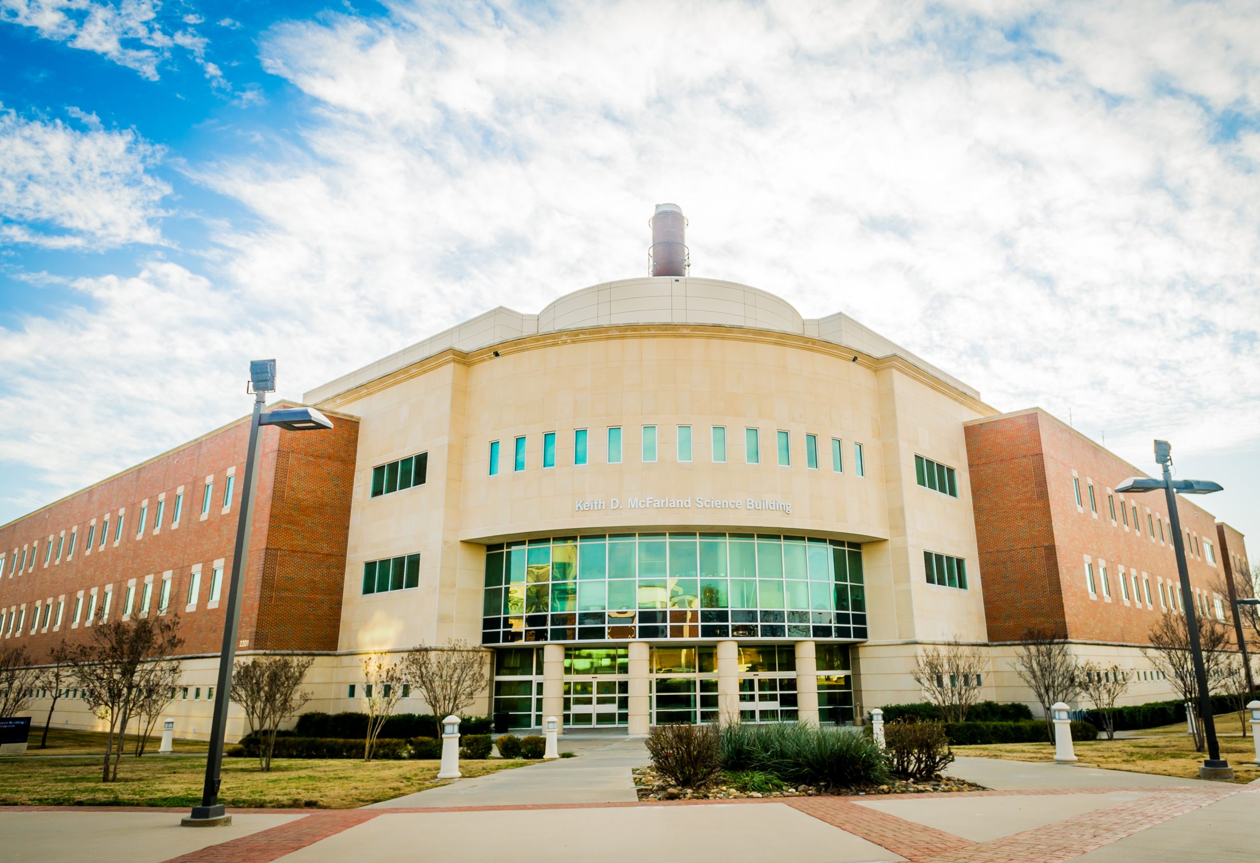 A big brick building with a title on the front. The sky is covered in clouds.