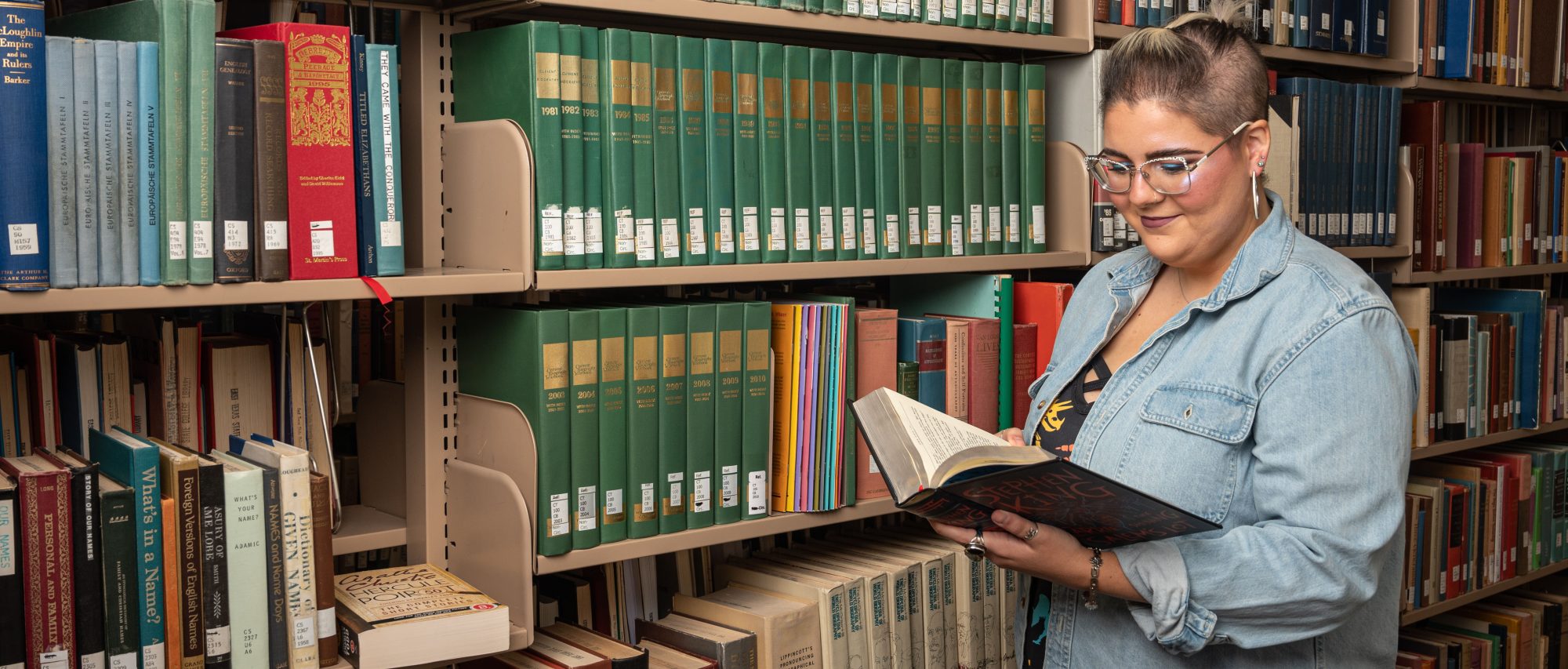 A female student looking at a book in the library smiling.