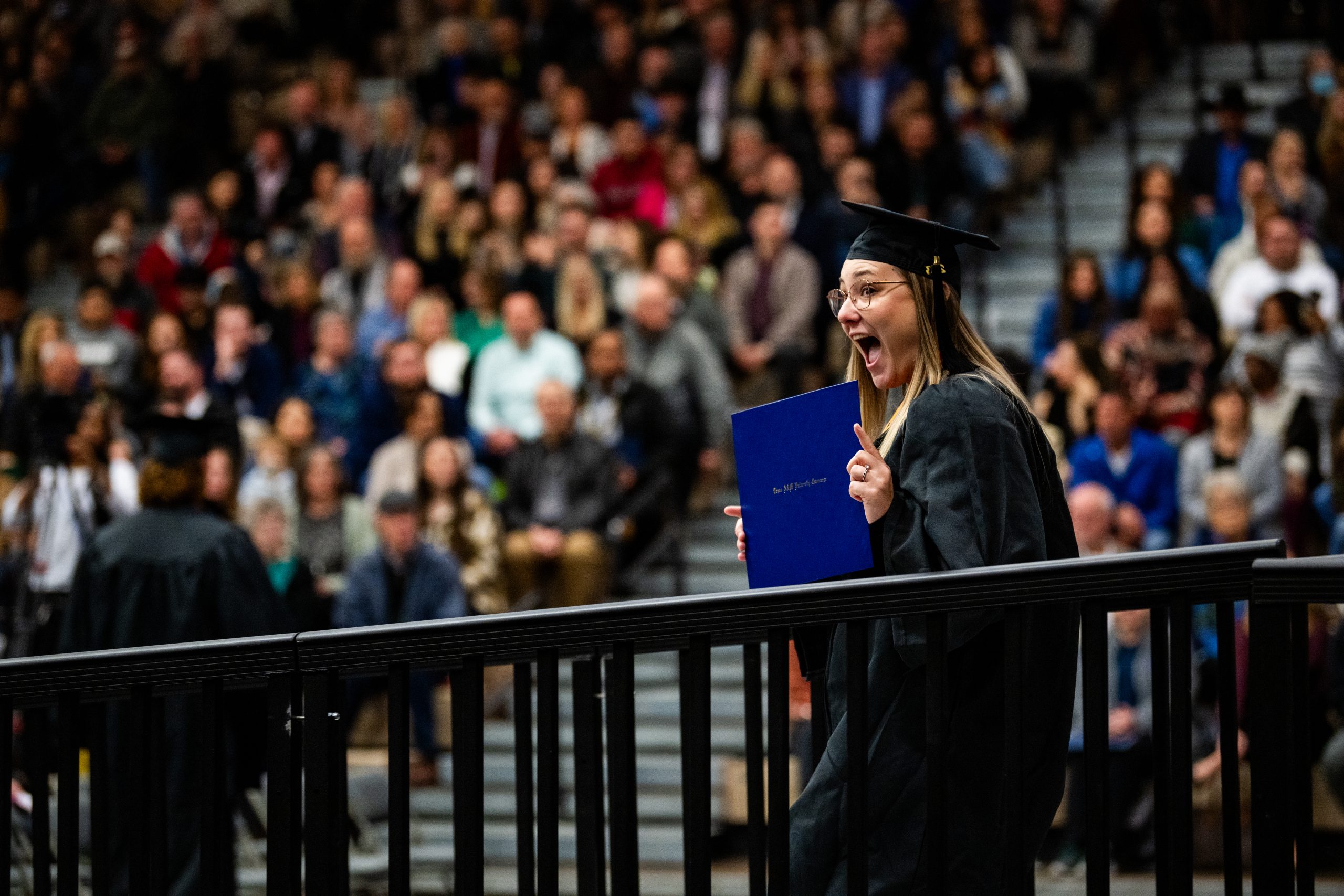 A female student holding her certificate to the rest of the graduates.