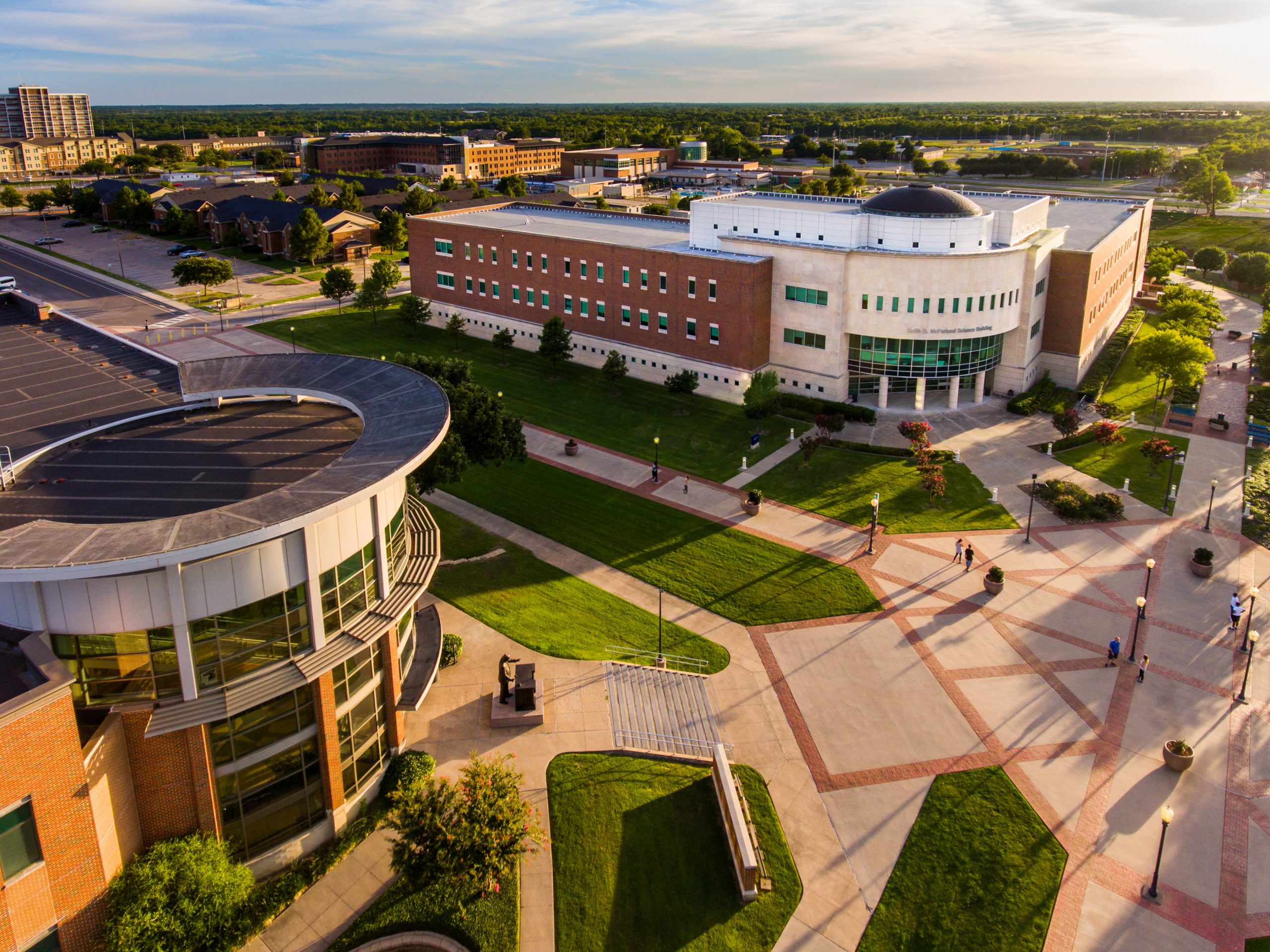 Aerial view of the East Texas A&M University campus, showcasing modern buildings, walkways, and green spaces under a clear sky.