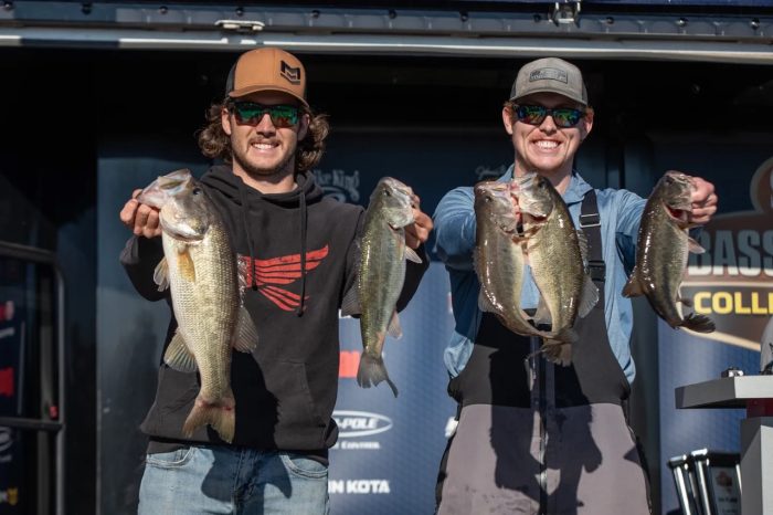 Two people hold a largemouth bass in each hand while posing for a photo.