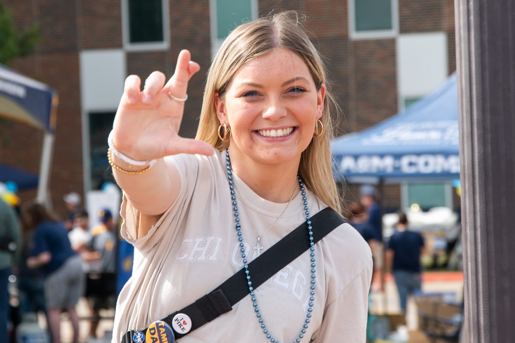 A female student wearing a light color shirt smiling at the camera, making the lions sign. In the background is other students.