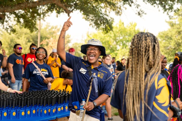 Group of students participating in Lion Walk. A student is shown holding a walking stick and waving.
