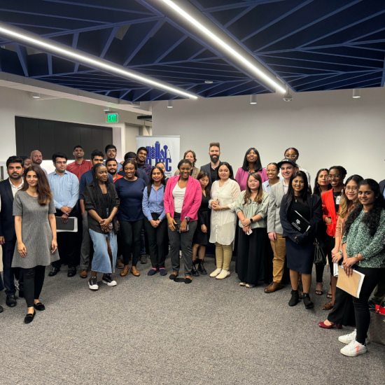 A large group of people stand posing for a photo in an office setting with a modern ceiling design. Some individuals are holding papers, and a cityscape logo is visible on the back wall. Everyone is dressed in business casual attire and smiling.