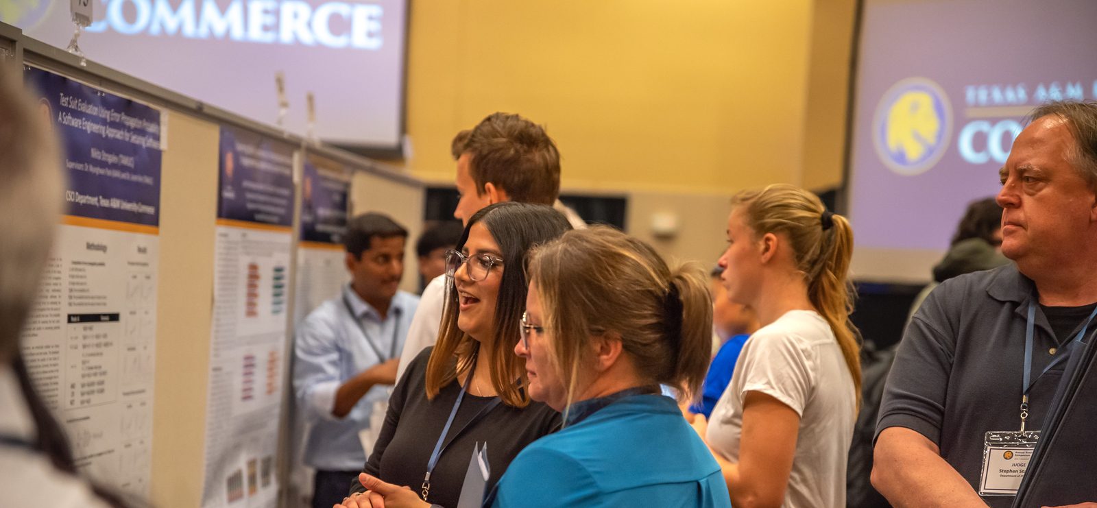Several students and symposium attendees view research project posters.
