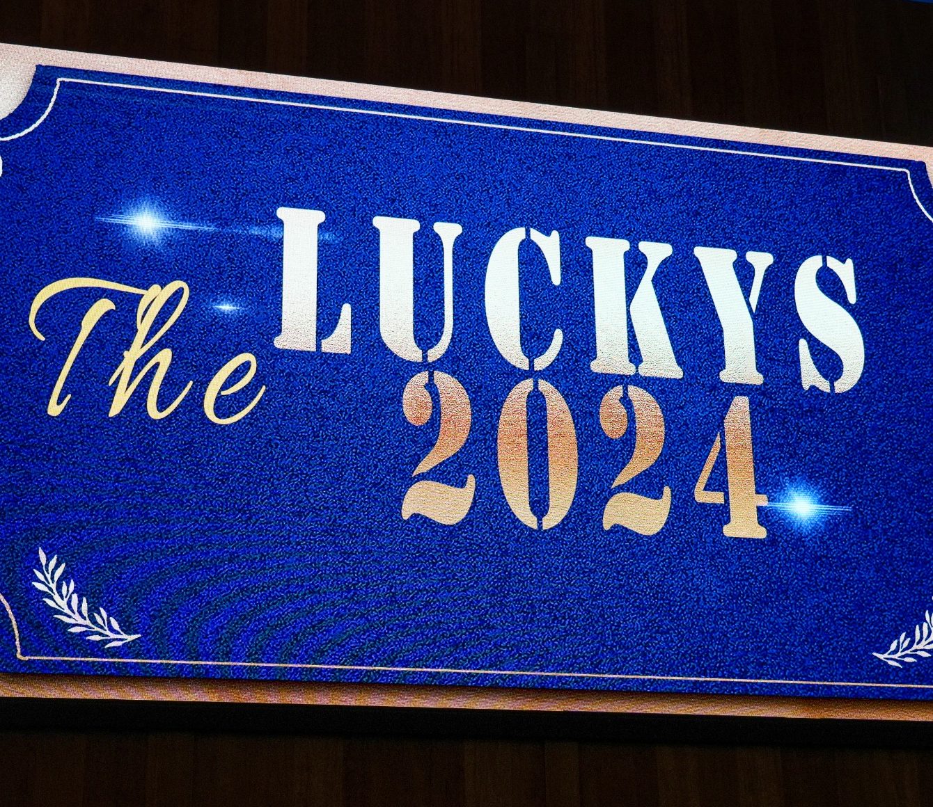 Sign welcoming guests to The Luckys 2024. Sign reads "The Luckys 2024" with blue background and white and gold lettering.