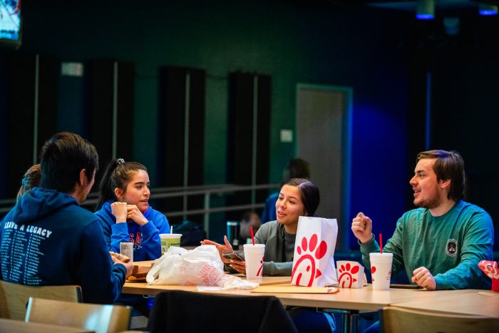A group of student sitting in a place where they can eat and on the table is chick fila.
