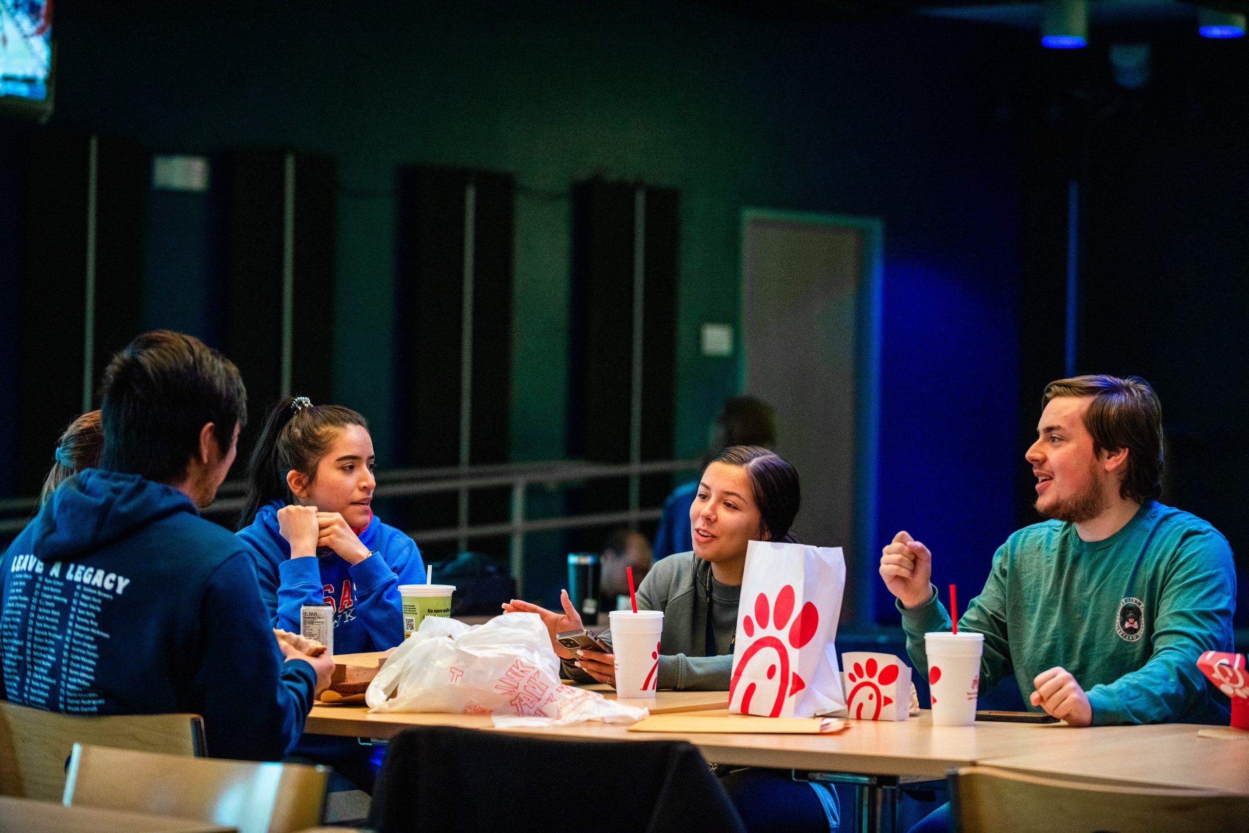 A group of student sitting in a place where they can eat and on the table is chick fila.