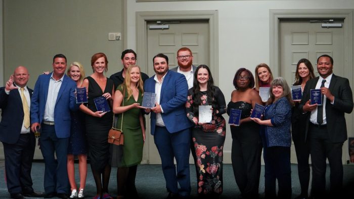 14 guests from the Night of Champions, dressed formally in suits and dresses, smile for the camera.