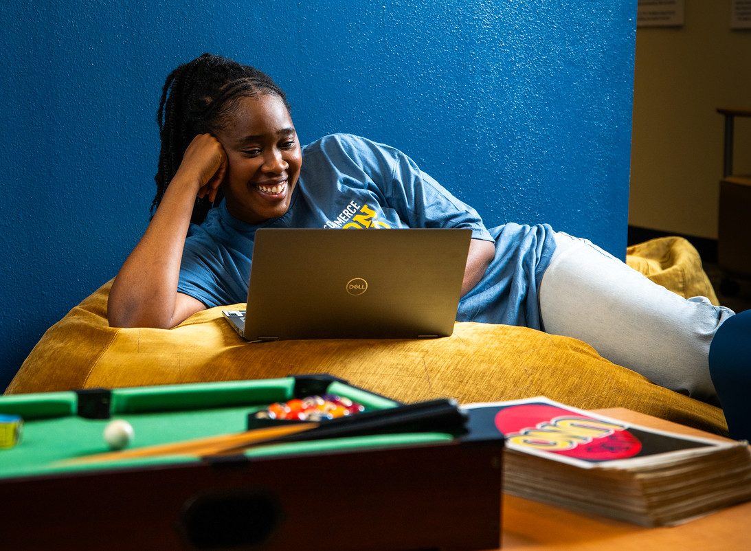 Girl lays on her side, propped up on her arm, as she looks at her laptop.