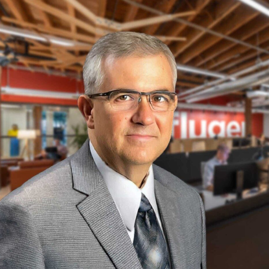A man faces the viewer with an office background behind him.