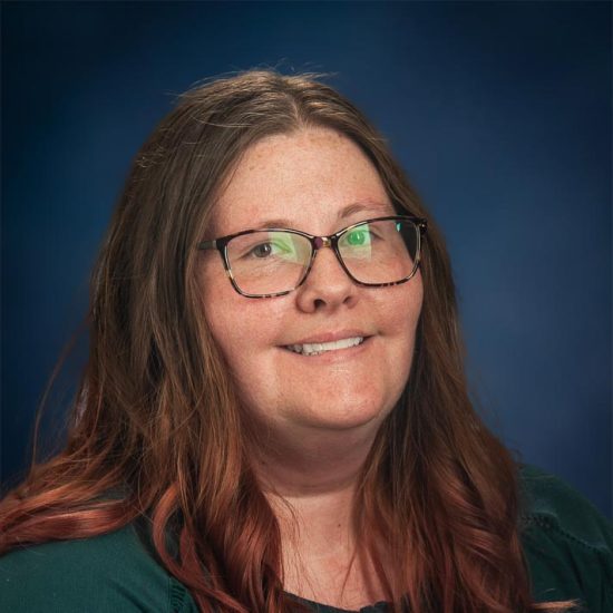 A smiling woman with long brown hair and glasses, wearing a dark green top, is set against a dark blue background.