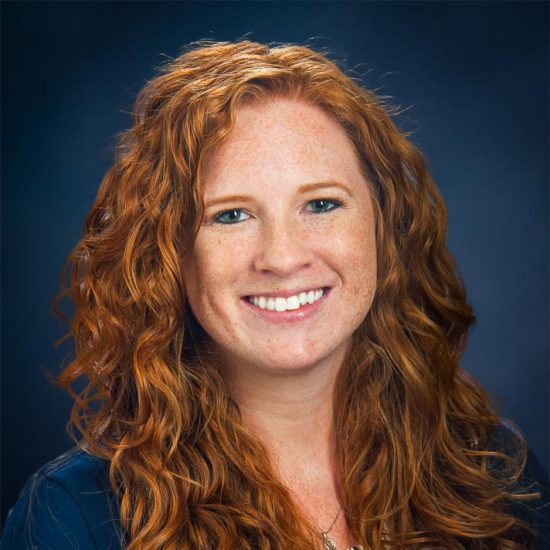 A smiling woman with curly red hair against a dark blue background.