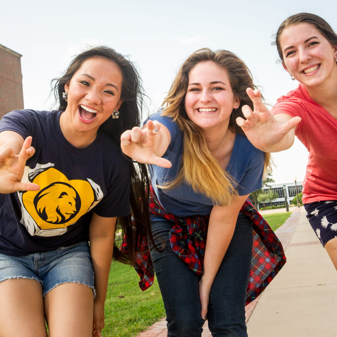 Three female students smiling while showing the leo hand sign.