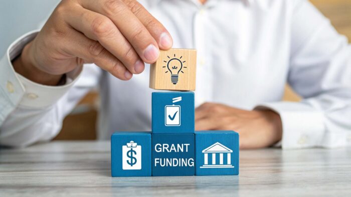 Hand stacking blocks. One block says "Grant Funding."