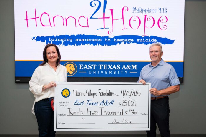 Two people hold a poster-size check, one on each side. Behind them, a screen reads "Hanna4Hope."