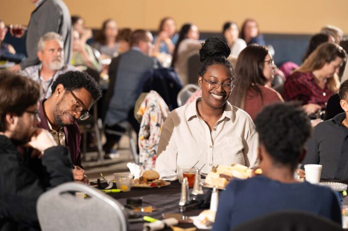 People sit around round tables set with diningware. They laugh and talk to each other.