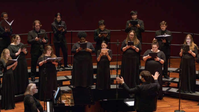 A director conducts a choir on stage during a concert.