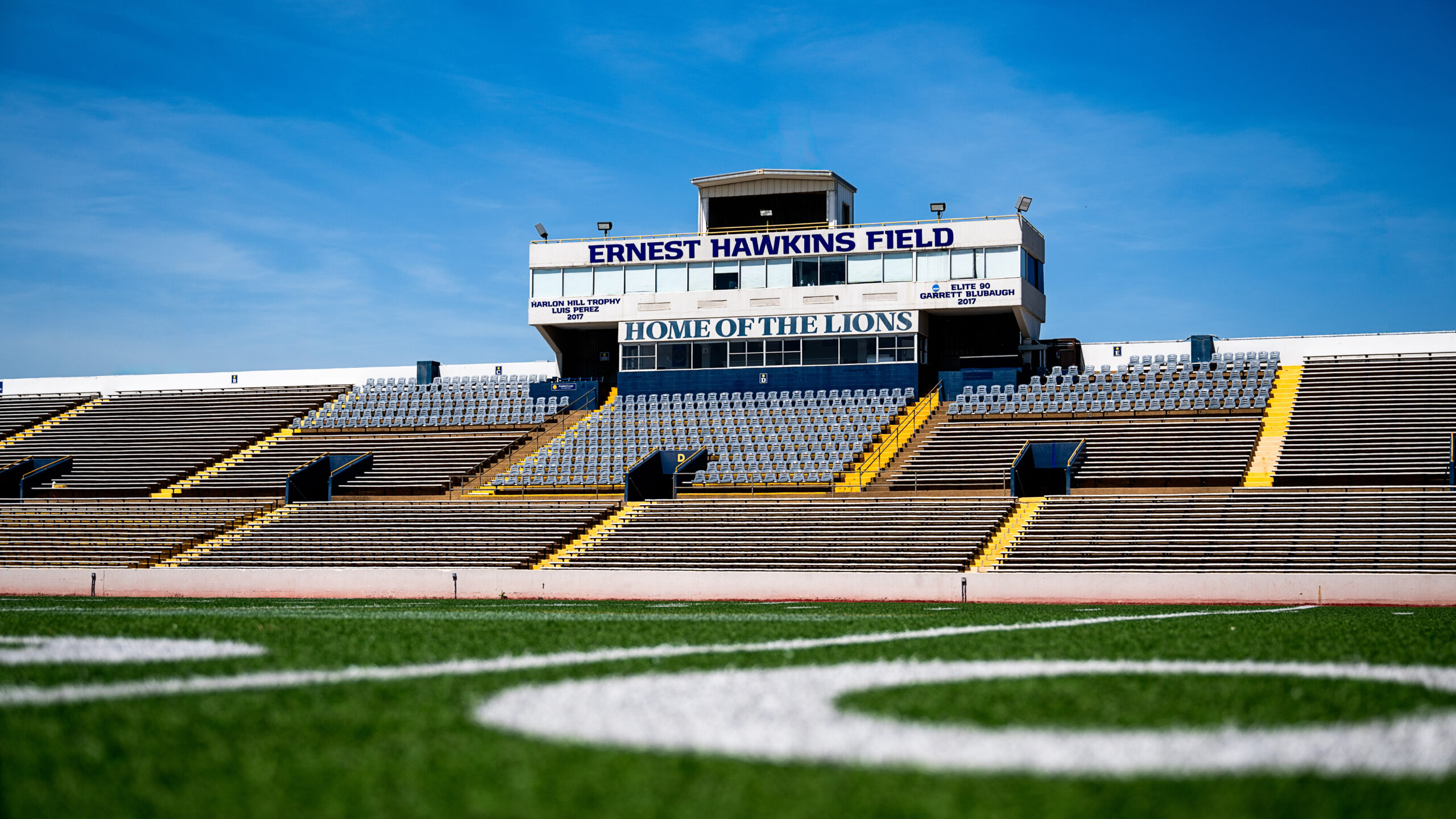 A football stadium photographed from midfield on a sunny day.