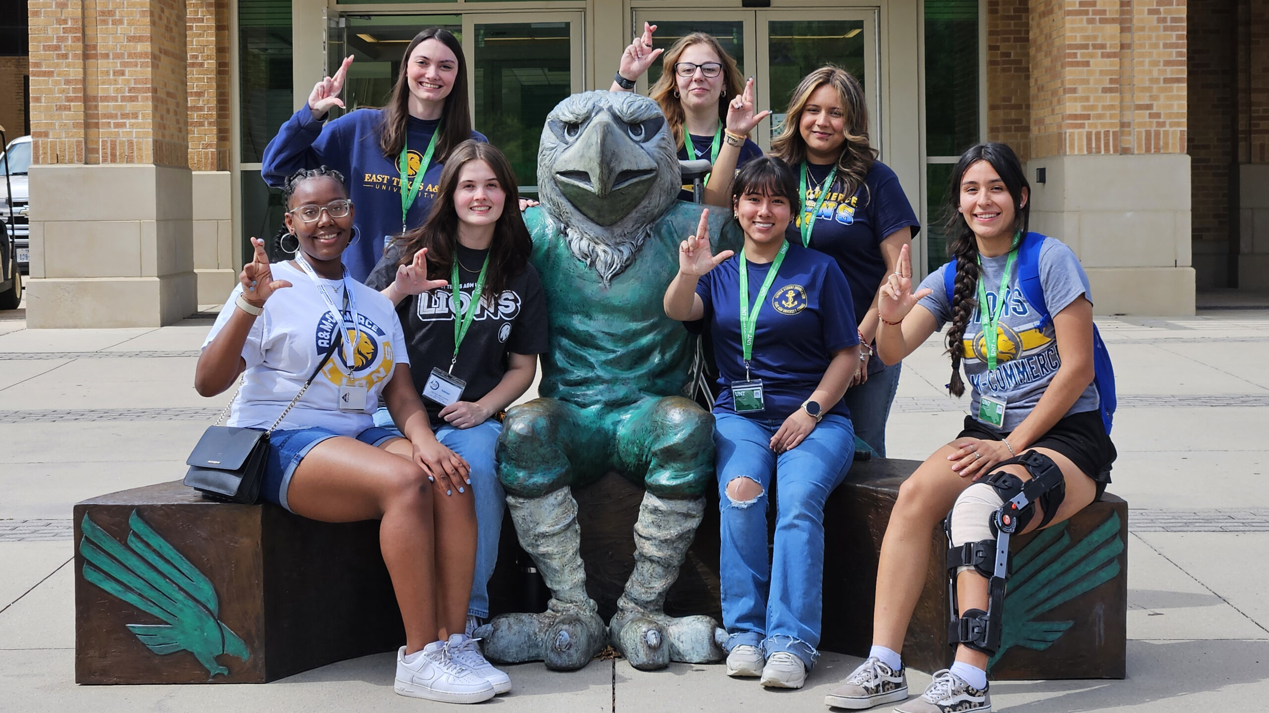 A group of college students sitting with a large eagle mascot statue on a college campus.