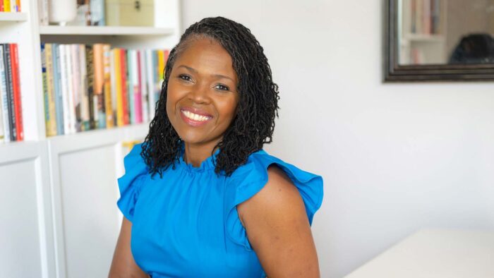 Woman in blue blouse smiling in front of a bookshelf.