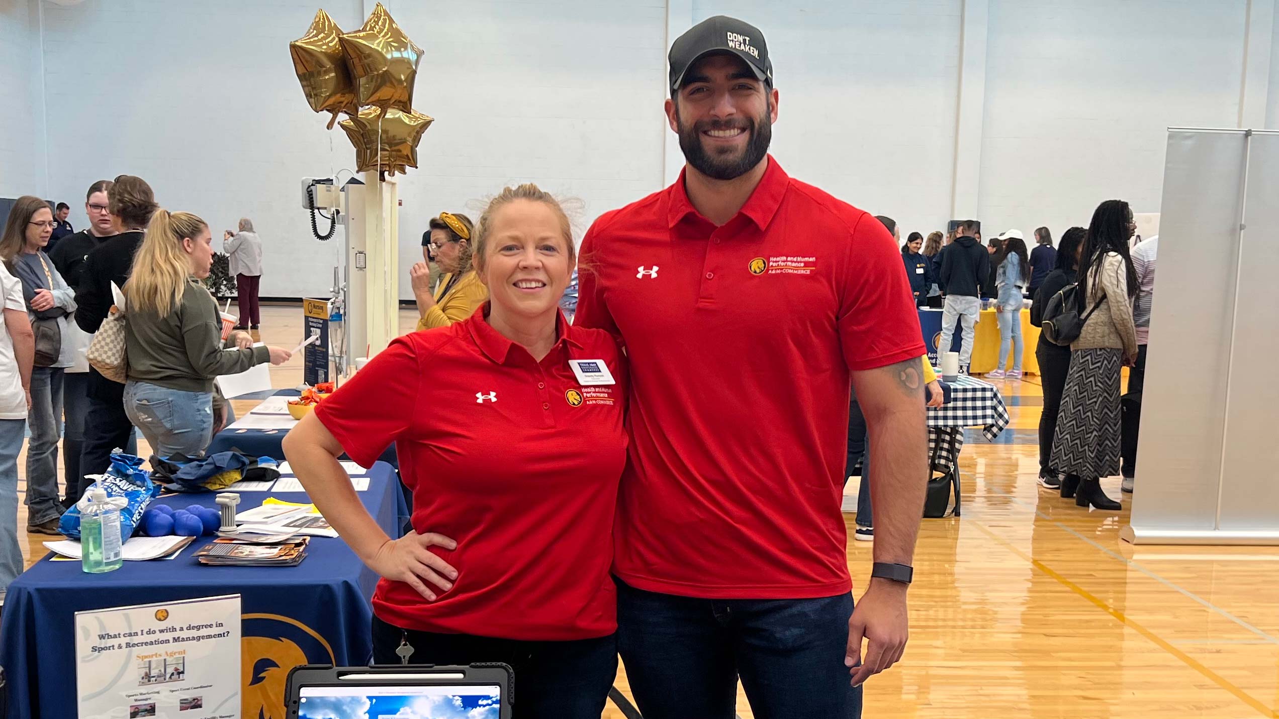 A man wearing a ballcap standing with a woman, both wearing red shirts with the East Texas A&M logo.