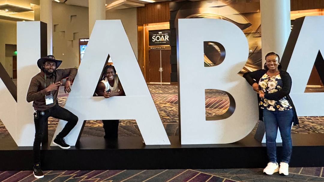 People in a convention center posing near large letters spelling NABA.