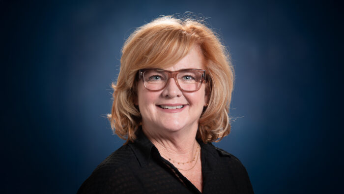 A headshot photo of a person on a dark blue background.