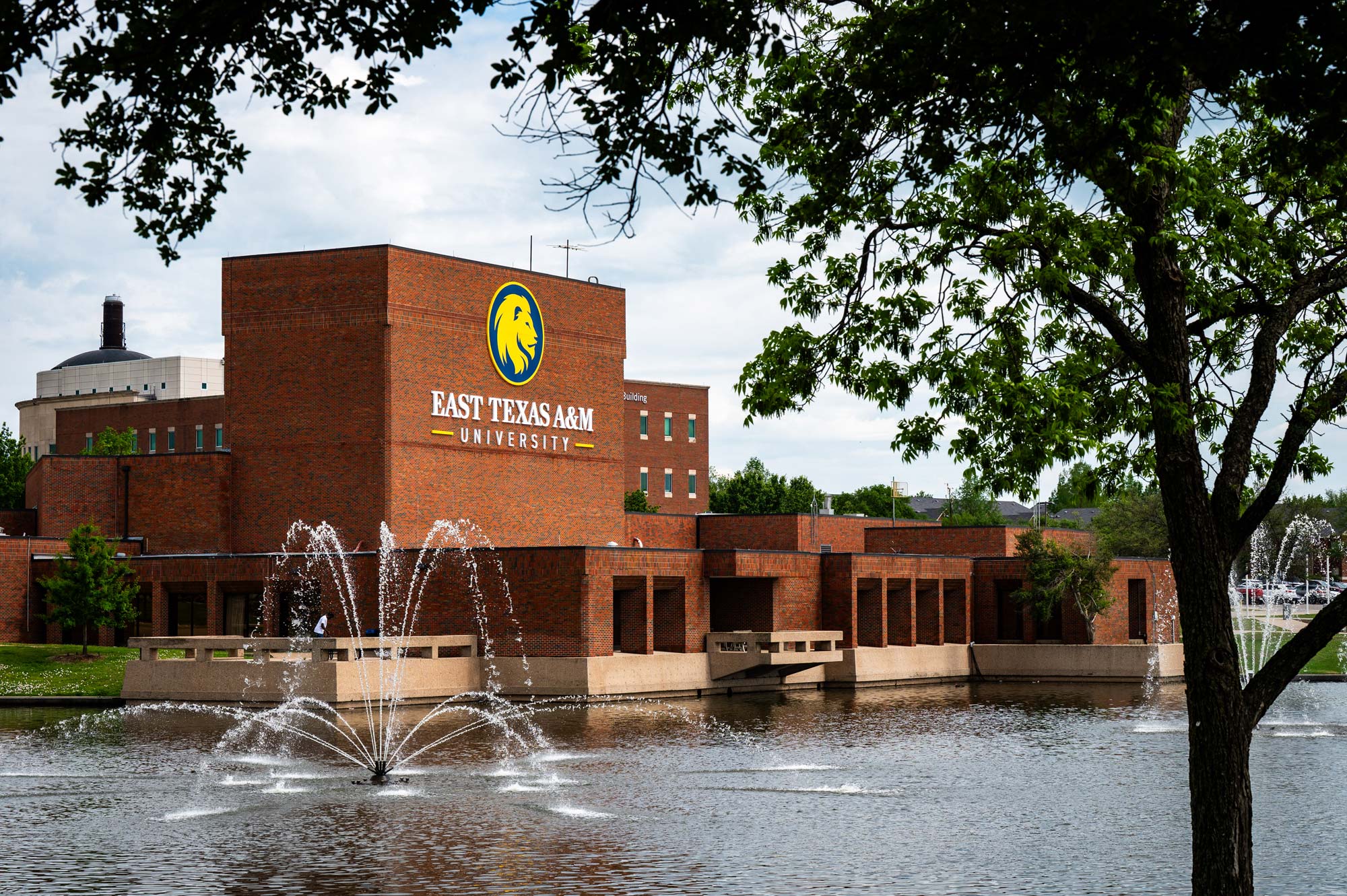 Brick university building is in the background with a pond in front of it, with a fountain.
