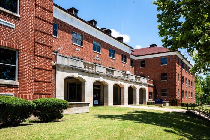 Photo shows exterior of a red brick building with gray archways along the front.