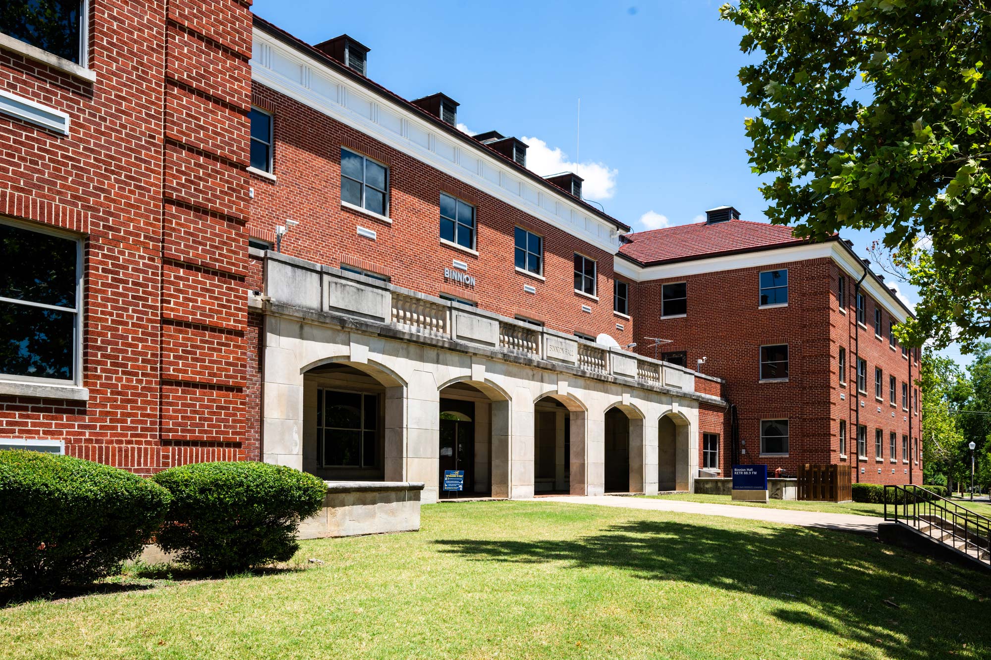 Photo shows exterior of a red brick building with gray archways along the front.