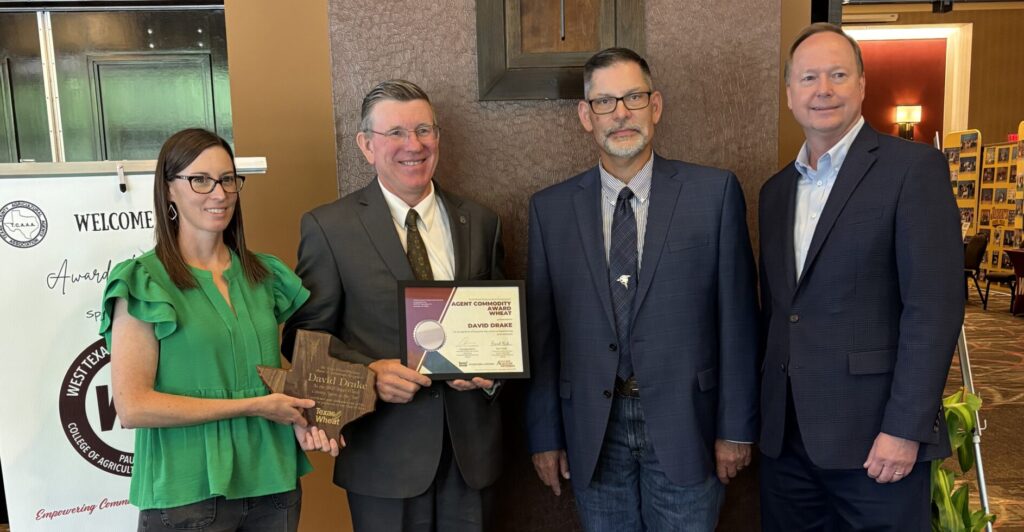 Four people stand shoulder to shoulder to pose for a photo. Two of the people are holding an award plaque.