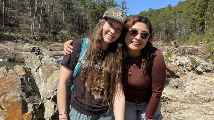Two people posing together in rugged outdoor setting.