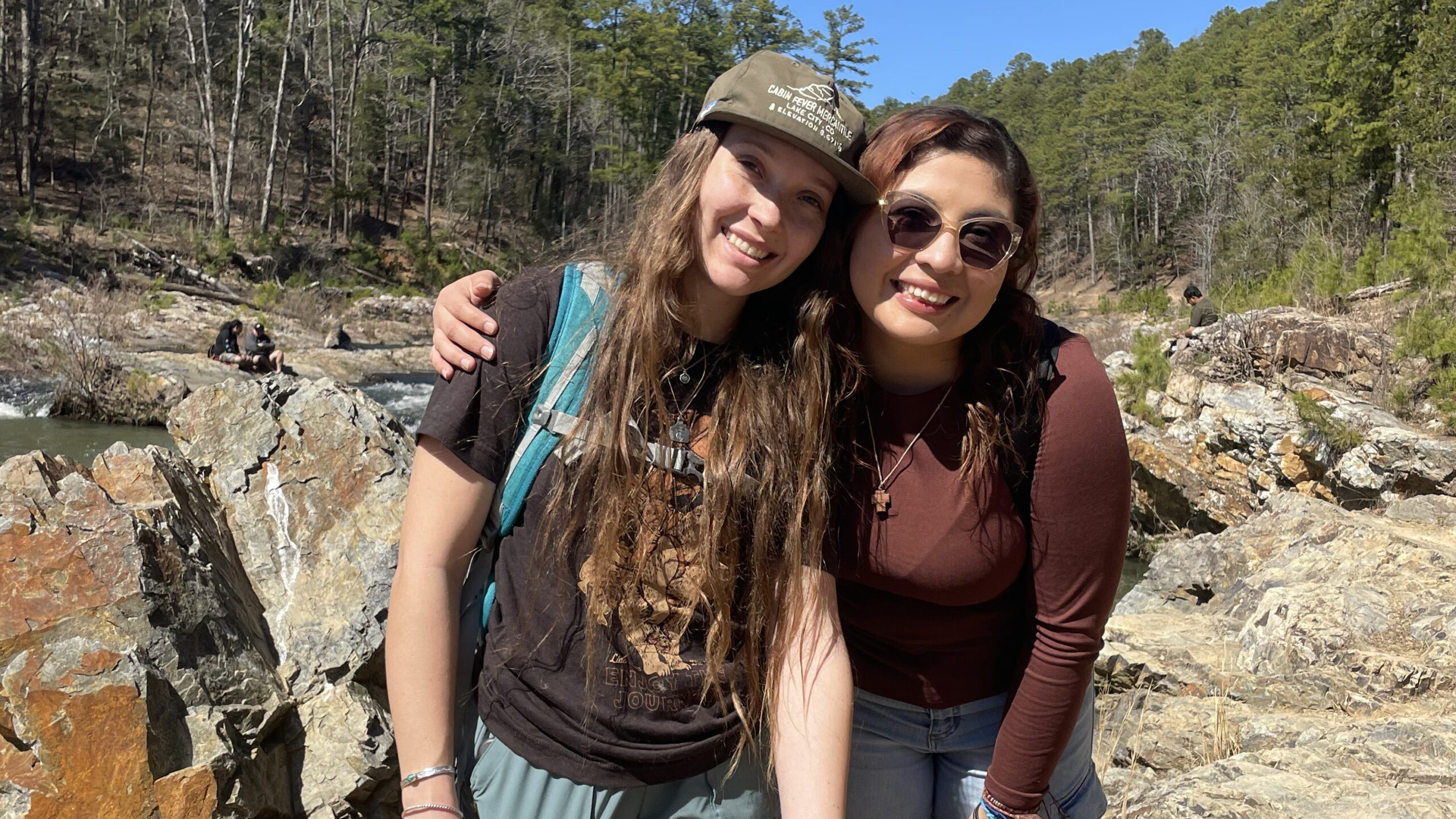 Two people posing together in rugged outdoor setting.